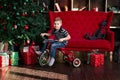 Smiling little boy riding bicycle in the room with christmas tree , new year presents , red coach, book shelf Royalty Free Stock Photo