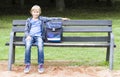 Smiling little boy sitting on a wooden bench with his backpack. Education, school, lifestyle, people concept Royalty Free Stock Photo