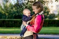 Child smiles in baby sling in hands of his mother during walking in park. Royalty Free Stock Photo