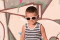 Smiling little boy wearing sunglasses and striped shirt on graffiti background Royalty Free Stock Photo