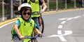 A smiling little boy is wering a helmet and a safety vest and riding a bicycle