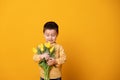 Smiling little boy on yellow studio background. Cheerful happy child with tulips flower bouquet Royalty Free Stock Photo