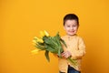 Smiling little boy on yellow studio background. Cheerful happy child with tulips flower bouquet Royalty Free Stock Photo