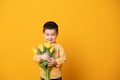 Smiling little boy on yellow studio background. Cheerful happy child with tulips flower bouquet Royalty Free Stock Photo