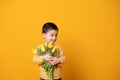 Smiling little boy on yellow studio background. Cheerful happy child with tulips flower bouquet Royalty Free Stock Photo