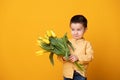 Smiling little boy on yellow studio background. Cheerful happy child with tulips flower bouquet Royalty Free Stock Photo