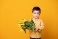 Smiling little boy on yellow studio background. Cheerful happy child with tulips flower bouquet Royalty Free Stock Photo