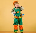 Smiling little builder boy in helmet and tool belt. Cute kid repairman in protective hard hat and overalls with tool Royalty Free Stock Photo