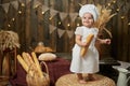 Smiling little caucasian girl baker stands and holds long loaf Royalty Free Stock Photo