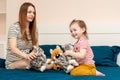 Smiling little child girl and her young mother playing with soft toy cats on a bed with dark blue linen Royalty Free Stock Photo