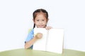 Smiling little child girl in school uniform show writing on blank notebook sitting at desk isolated over white background Royalty Free Stock Photo