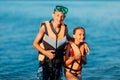 Happy, smiling little children, a boy and a girl, dressed in swimming goggles and life jackets, stand in the sea and look at the Royalty Free Stock Photo