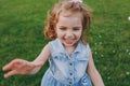 Smiling little cute child baby girl in denim dress pointing hand on camera, have fun on green grass lawn in park. Mother Royalty Free Stock Photo