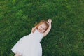 Smiling little cute child baby girl in light dress lie on green grass lawn, showing thumb up in park. Mother, little kid Royalty Free Stock Photo