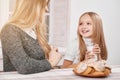 Smiling little daughter sits kepping milk glass near mother.