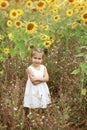 A smiling little dreaming girl with funny tails stands in a meadow with sunflower flowers and looks thoughtfully away. Royalty Free Stock Photo