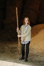 Smiling little ginger girl standing inside a barn with pitchfork in hands Royalty Free Stock Photo
