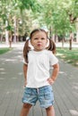 Smiling little girl in blank white t-shirt standing in park