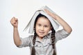 Smiling little girl with braided pigtails shows her fist while holding a large book over her head Royalty Free Stock Photo