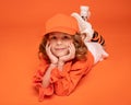 Smiling little girl in a cap and fashionable clothes lying down on floor in studio on orange background. Mock up
