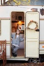 Smiling little girl in casual clothes standing on porch RV house in garden. Cute young girl stand near trailer door. Child in cozy