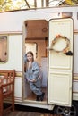 Smiling little girl in casual clothes standing on porch RV house in garden. Cute young girl stand near trailer door. Child in cozy