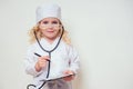 Smiling little girl in doctor uniform with medical tools stethoscope writing something to clipboard on white background Royalty Free Stock Photo