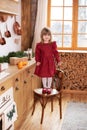 Smiling little girl in dress cooking pie. Happy child stand on chair in kitchen in decorations with Christmas tree and gift. Kid h Royalty Free Stock Photo