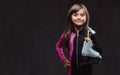 Smiling little girl dressed in sportswear holds ice skates on a shoulder. Isolated on dark textured background. Royalty Free Stock Photo