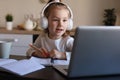 Smiling little girl in headphones handwrite study online using laptop at home Royalty Free Stock Photo