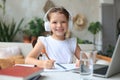 Smiling little girl in headphones handwrite study online using laptop at home