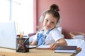 Smiling little girl in headphones handwrite study online using laptop at home