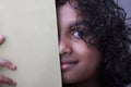 A smiling little girl with her face half covered by a book