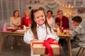 Smiling little girl holding wrapped gift box during festive dinner, celebrating holiday with her big family at home Royalty Free Stock Photo