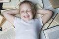 A smiling little girl lies with closed eyes on a pile of open books. Top view. Education and training. Close-up