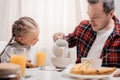 smiling little girl looking at father pouring milk into bowl with flakes Royalty Free Stock Photo