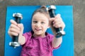 Smiling little girl lying on mat and exercising with dumbbells Royalty Free Stock Photo