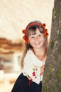 Smiling little girl in the national Ukrainian Hutsul costume and in a wreath looks out from behind a tree Royalty Free Stock Photo