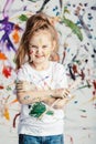Smiling little girl with painting brush on messy background.
