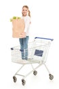 smiling little girl with paper bag standing in shopping cart Royalty Free Stock Photo