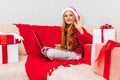 Smiling little girl in Santa Claus hat  uses laptop and meets Christmas (New Year) at home  sitting on the couch Royalty Free Stock Photo