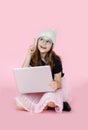 Smiling little girl sitting on the floor with legs crossed and posing with the laptop. studio shot isolated on pink. Royalty Free Stock Photo