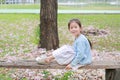 Smiling little girl sitting on wood logs against falling pink flower in the summer garden Royalty Free Stock Photo