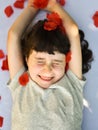 Smiling little girl squints as rose petals fall on her