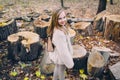 Smiling little girl stand next to wooden stumps in the forest at autumn day. Royalty Free Stock Photo