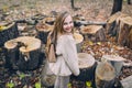 Smiling little girl stand next to wooden stumps in the forest at autumn day.