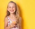 Smiling little girl in summer attire looking at camera holding glass of fresh carrot juice in hand. Waist up shot