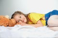 A smiling little girl with a teddy bear is lying on a white clot