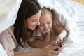 Smiling little girl using cell playing with mom at home