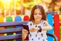 Happy kid with trendy gadgets synchronizing smartwatch with smartphone while sitting on bench in park Royalty Free Stock Photo